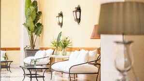 Une chambre d’hôtel comprenant un lit, deux chaises, une table avec un vase de fleurs et deux lampes fixées au mur.