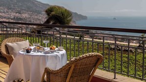 Une table dressée pour deux personnes, avec vue sur la mer et les collines.