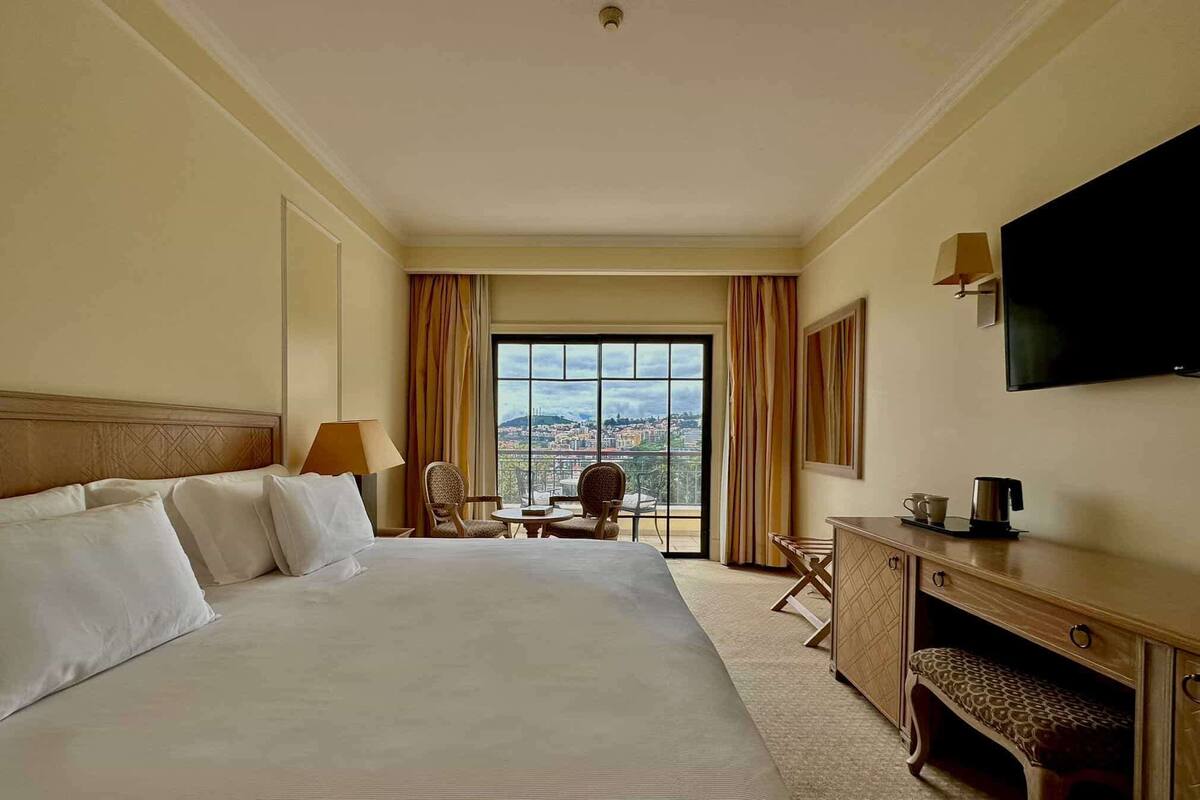 Une chambre d’hôtel avec un grand lit, un bureau, une chaise, une petite table et un téléviseur.