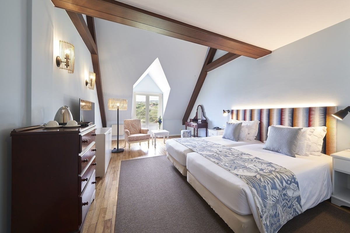 A bedroom with a large bed, a desk, a chair, and a view of the outdoors.