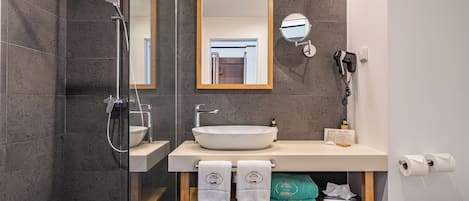 A modern bathroom with a glass-enclosed shower, a large mirror, a sink with a vessel basin, and a wooden shelf with towels.