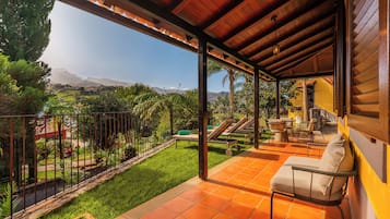 A covered patio with a view of a lush garden and distant mountains.