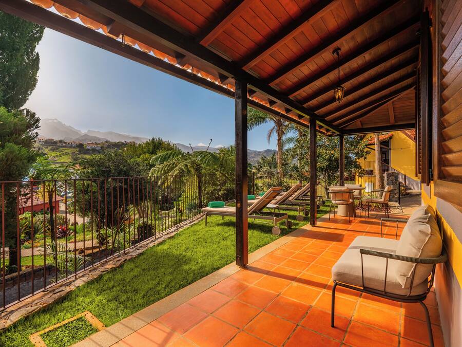 A covered patio with a view of a lush garden and distant mountains.