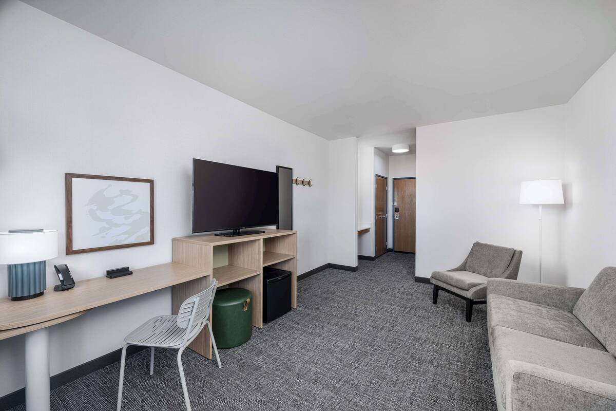 A hotel room with a desk, television, and seating area.
