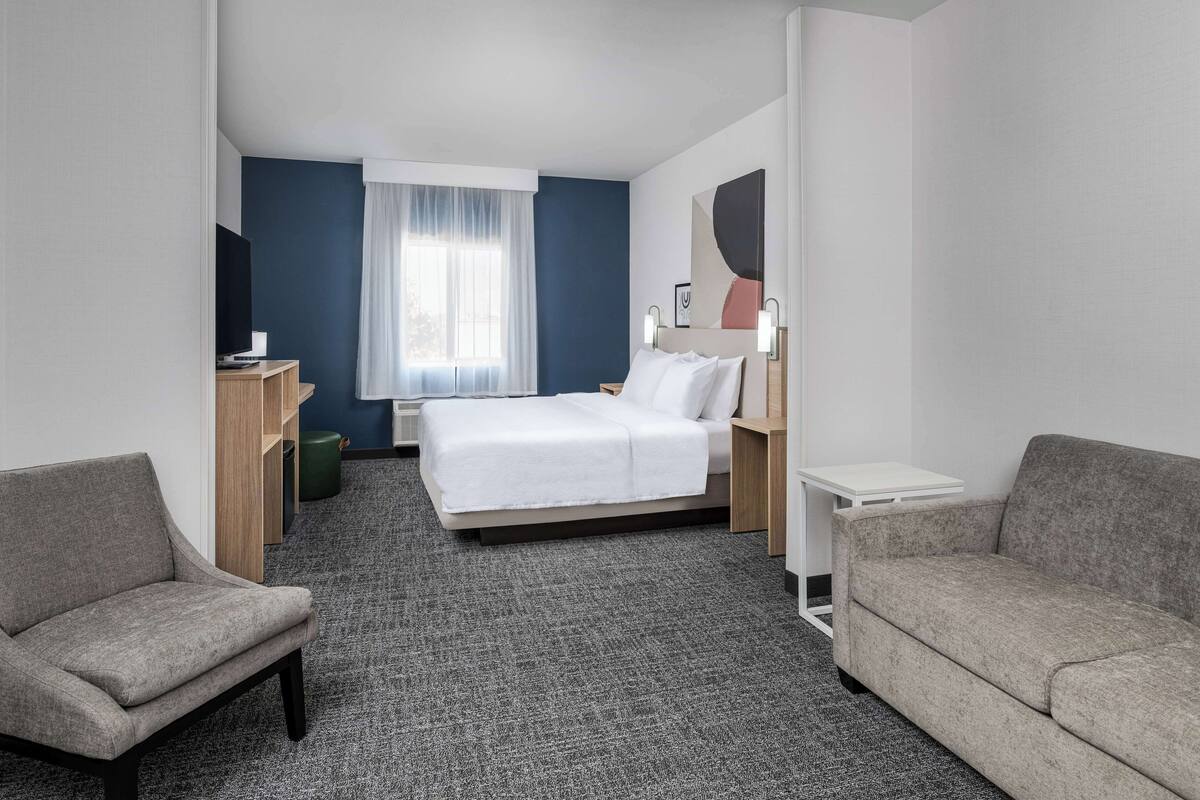 A hotel room with a bed, two armchairs, a desk, and a window with curtains.
