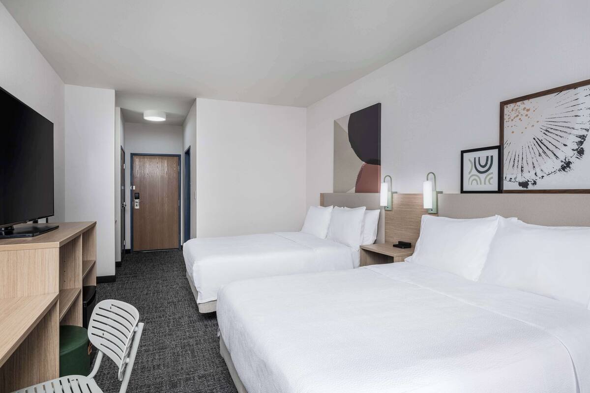 A hotel room with two beds, a desk with a television, a chair, and artwork on the wall.