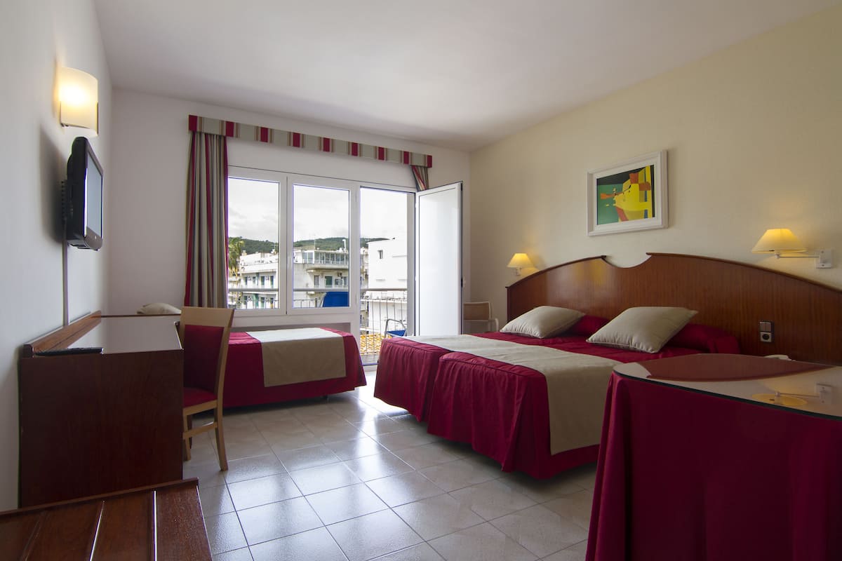 A hotel room with two beds, a desk, a chair, and a large window with a view of buildings.