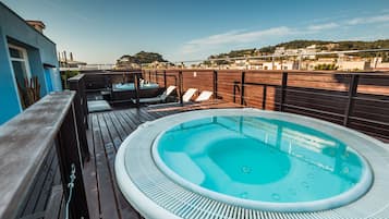 A rooftop pool area with a hot tub, wooden deck, and lounge chairs.