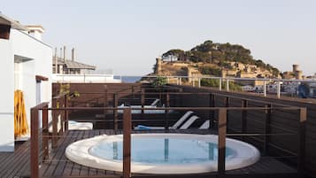 A rooftop deck with a hot tub, wooden railings, and a view of a historic hilltop fortress.
