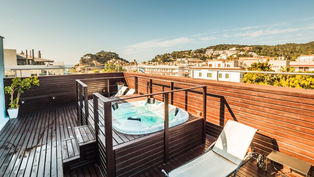 Una terraza en la azotea con jacuzzi, piso de madera y vistas a un paisaje urbano.