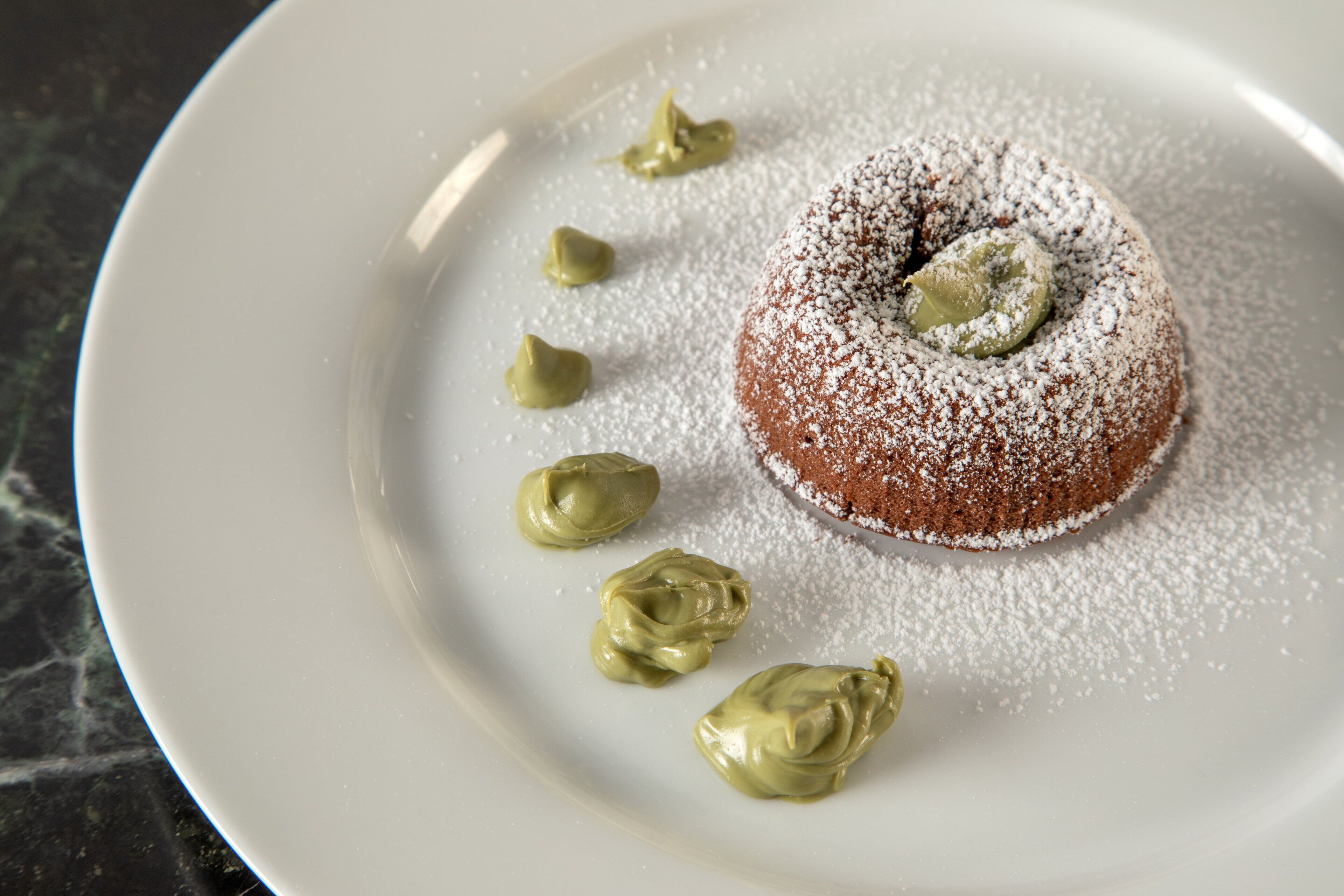 A dessert on a plate with powdered sugar and a dollop of green cream.