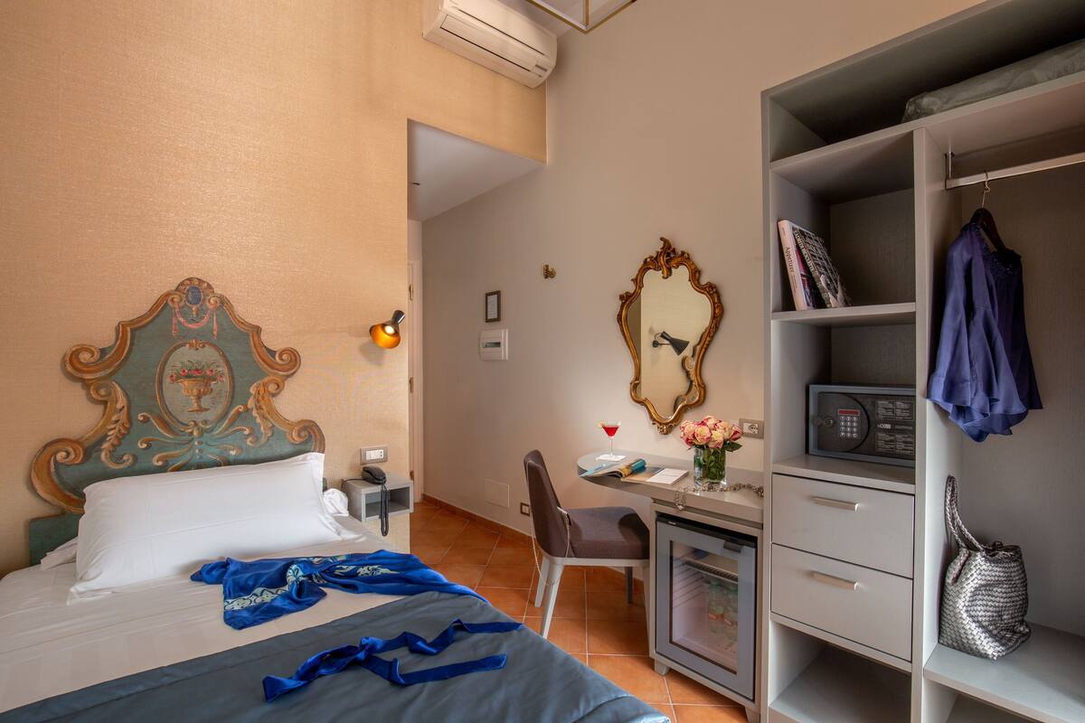 Hotellihuone, jossa on sänky, työpöytä, tuoli, vaatekaappi ja peili.