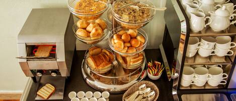 A buffet setup with various food items, including bread, pastries, and beverages.