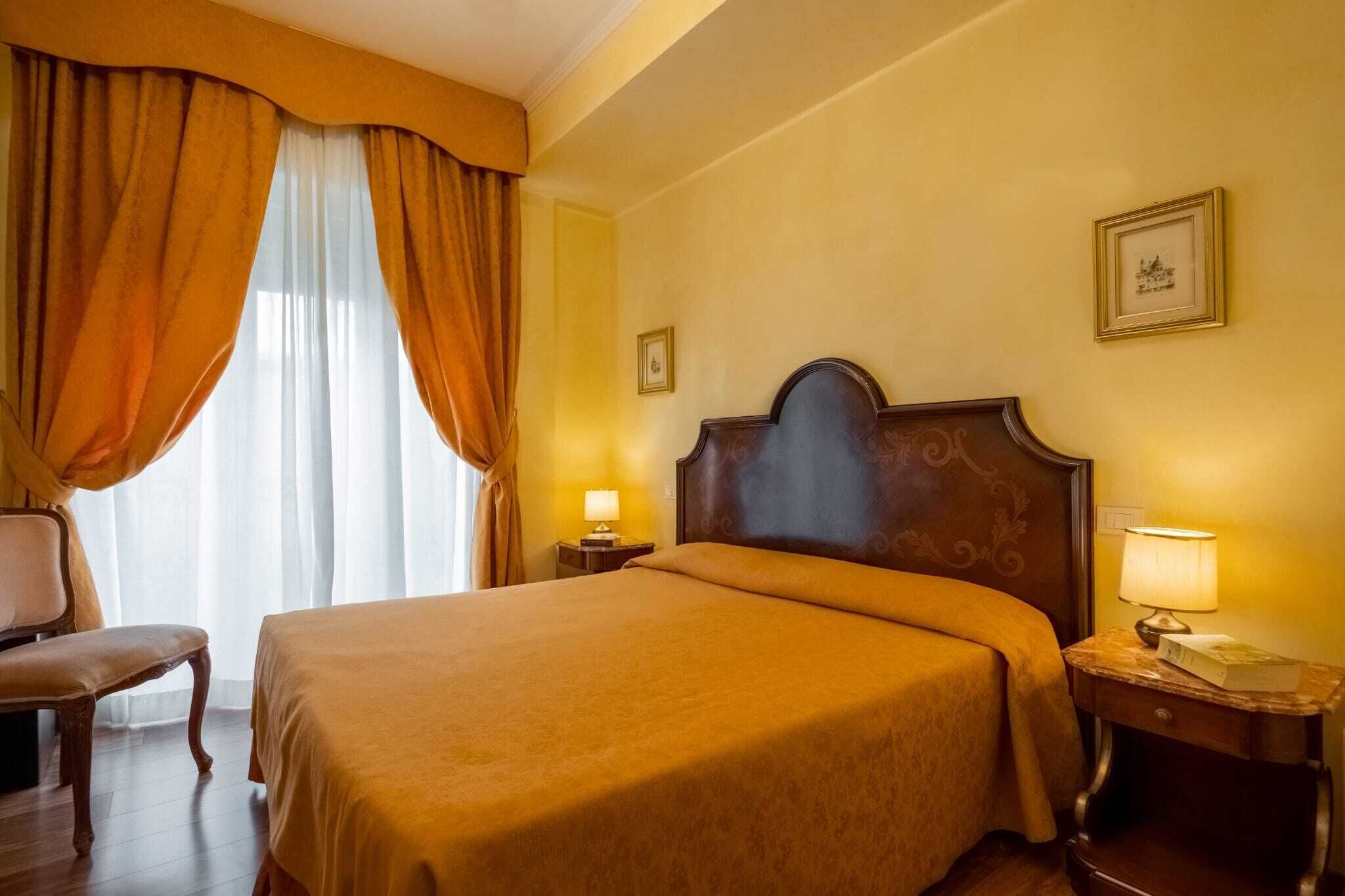 Ein Hotelzimmer mit einem großen Bett, einem Sessel, einem Nachttisch mit Lampe und einem Fenster mit Vorhängen.
