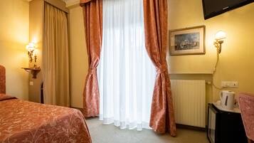 A hotel room with a bed, curtains, a painting, a wall-mounted TV, and a radiator.