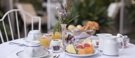 A breakfast table set with plates of fruit, a pitcher, and a vase with flowers.