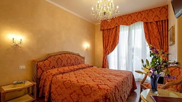 Ein Hotelzimmer mit einem großen Bett, einer Kristallleuchtre, einem Glastisch und einer Vase mit Blumen.