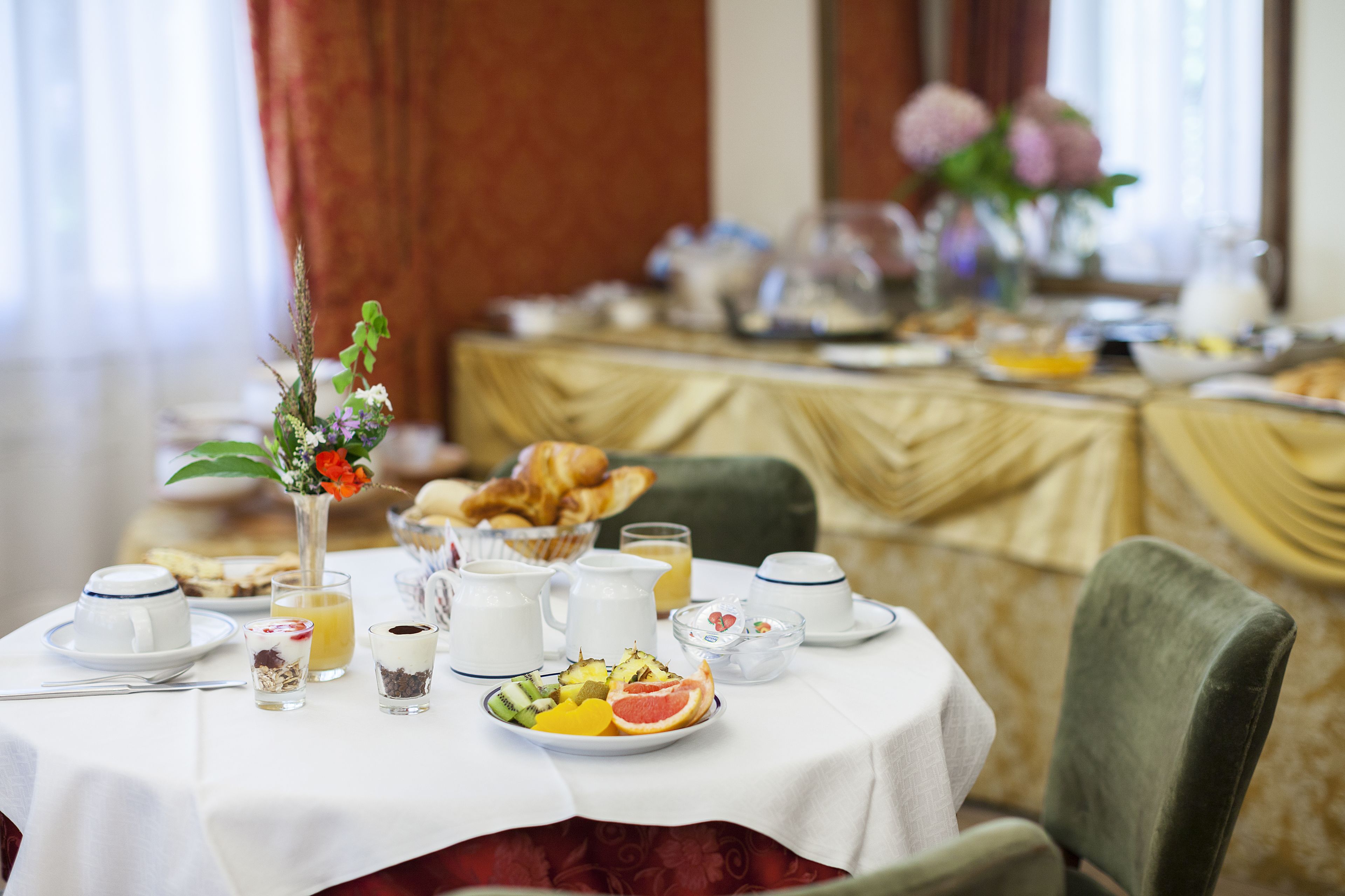 Ein Frühstückstisch reichhaltig gedeckt mit Früchten, Gebäck und Getränken.