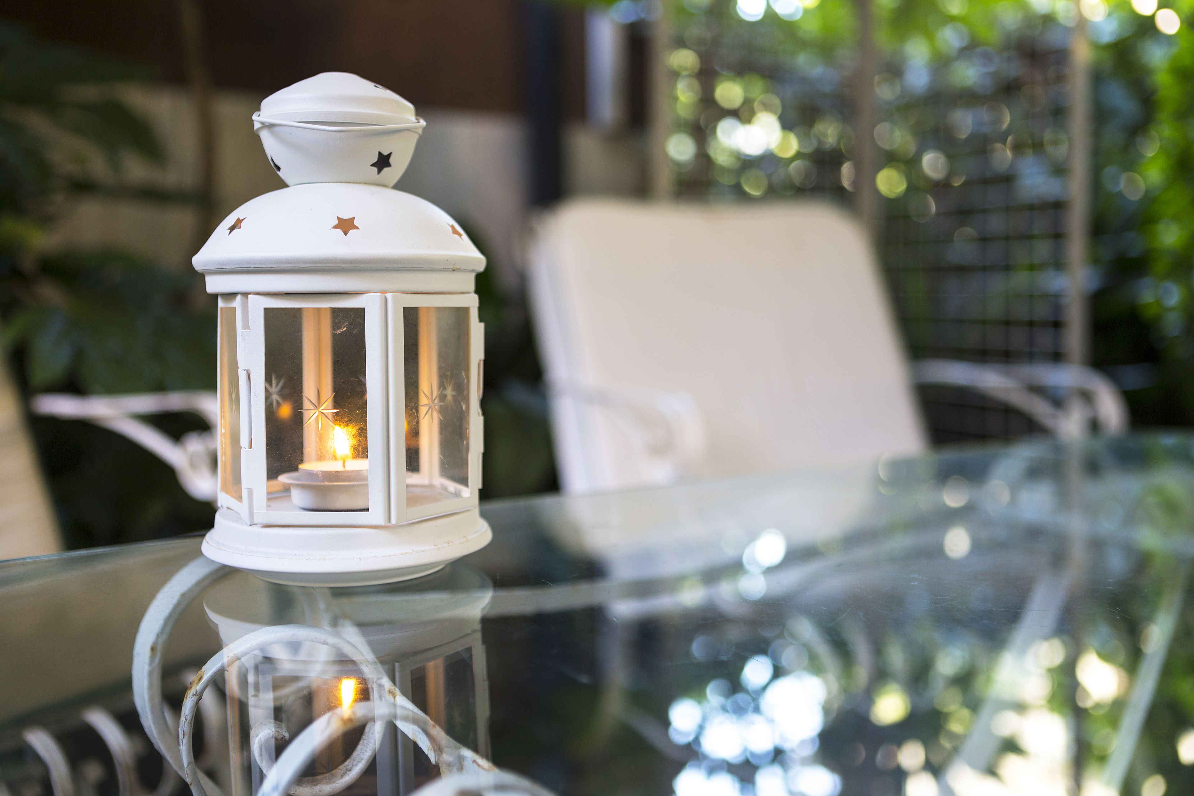 A white lantern with a lit candle on a glass table.