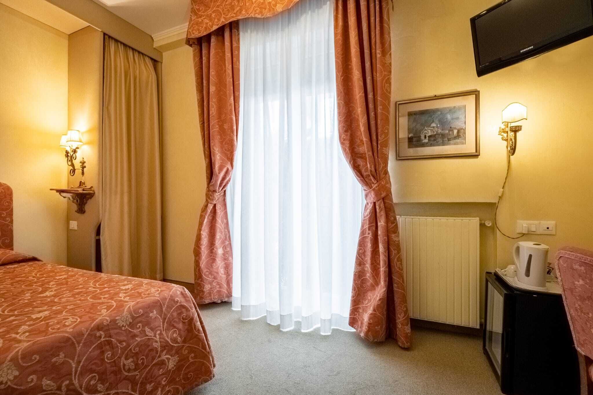 A hotel room with a bed, a radiator, a television, and a wall-mounted lamp.