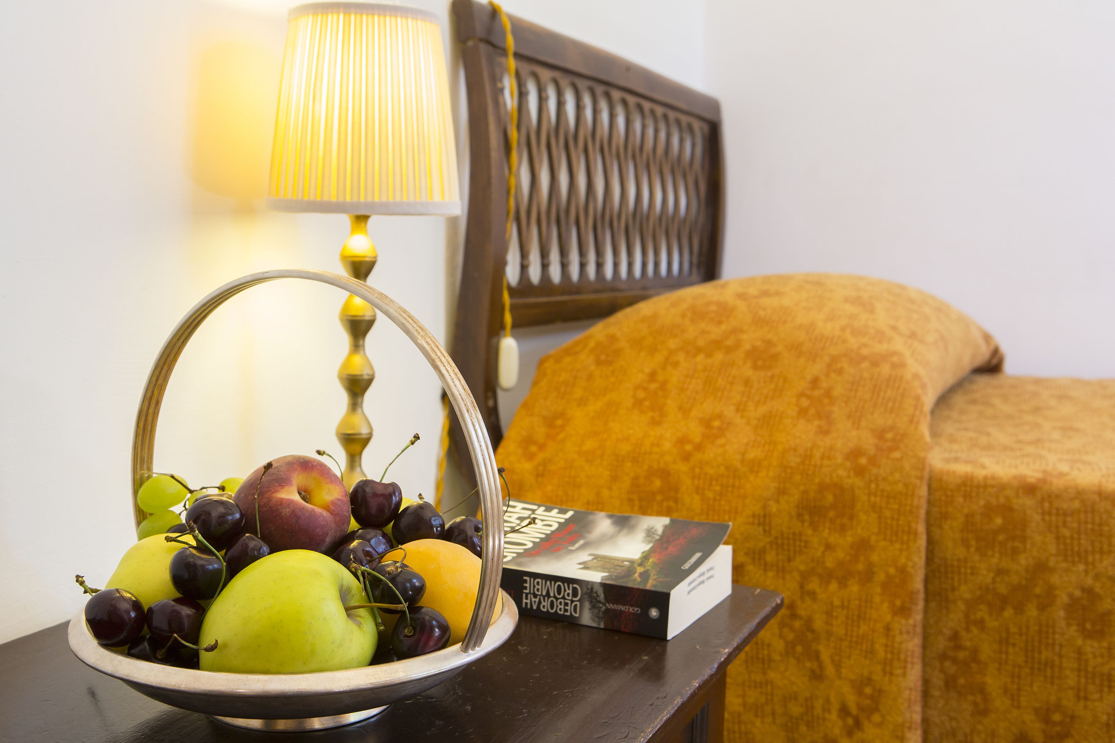 Eine Obstschale mit Äpfeln und Trauben auf einem Nachttisch neben einem Buch und einer Lampe.
