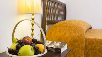 Un panier de fruits contenant des pommes et des raisins, posé sur une table de chevet, à côté d’un livre et d’une lampe.
