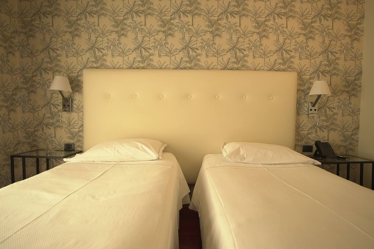 A hotel room with two single beds, a large headboard, and two bedside tables with lamps.