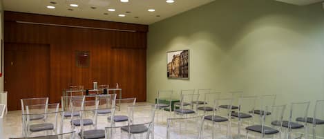 Un salón de conferencias con filas de sillas de plástico transparente, un panel de pared de madera e iluminación empotrada en el techo.