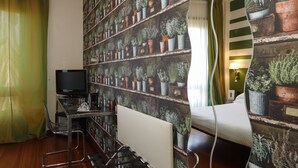 Habitación de hotel con una cama, un escritorio y un televisor, y una pared decorada con plantas en macetas.