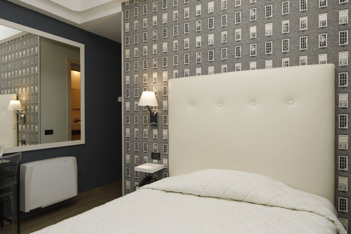 A hotel room with a large bed, a mirror, a small table, and a wall with a brick pattern.