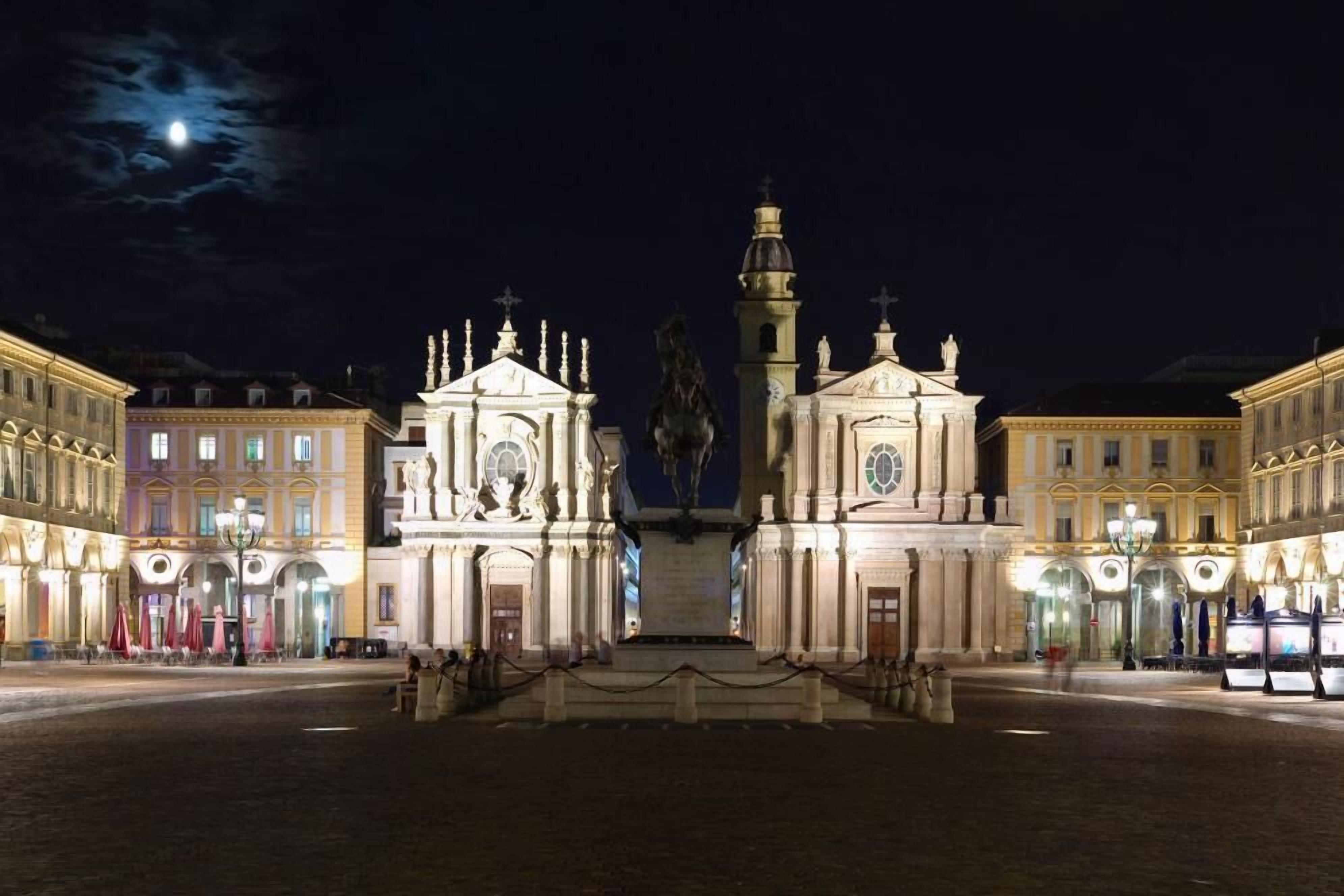A square with a central monument, surrounded by classical buildings with illuminated facades.
