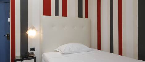 Una habitación de hotel con una cama, una mesita de noche con lámpara y una pared a rayas verticales.
