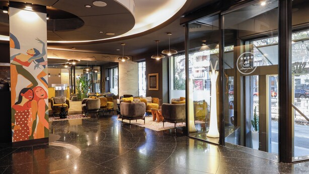 Un vestíbulo moderno con techo curvo, puertas de vidrio que dan al exterior y una zona de estar con sofás y sillones.