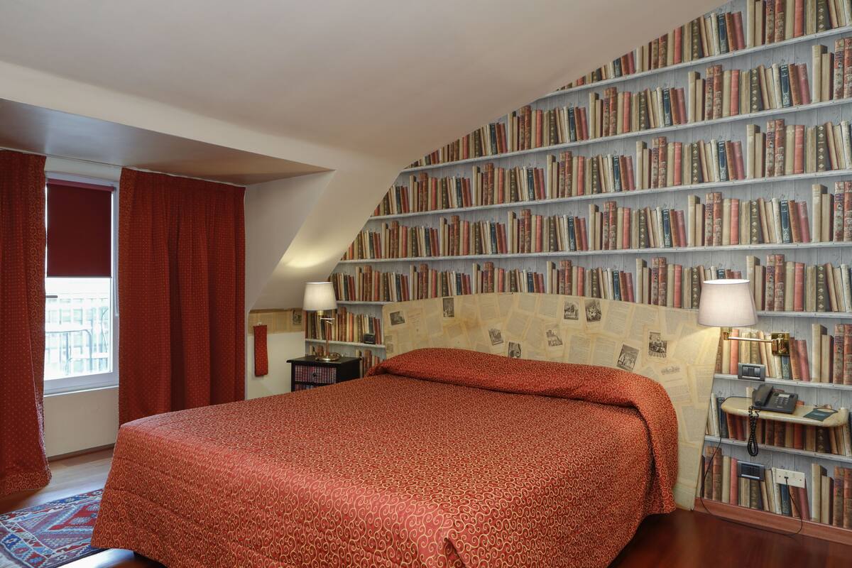 A bedroom with a large bed, a bookshelf, and a window with curtains.