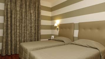 Habitación de hotel con dos camas, paredes a rayas, una cortina y una mesita de noche con lámpara.