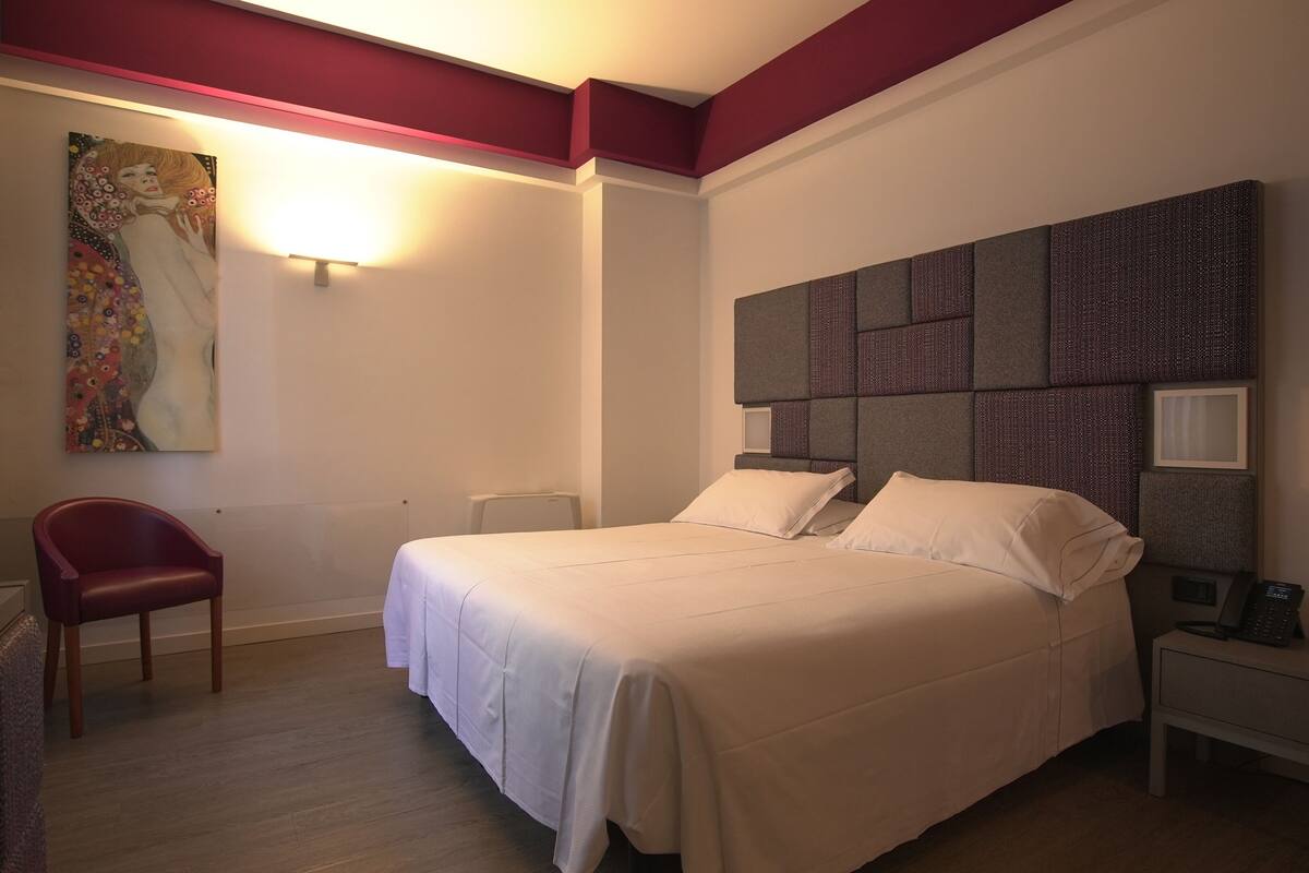 A hotel room with a large bed, a desk, a chair, and a painting on the wall.