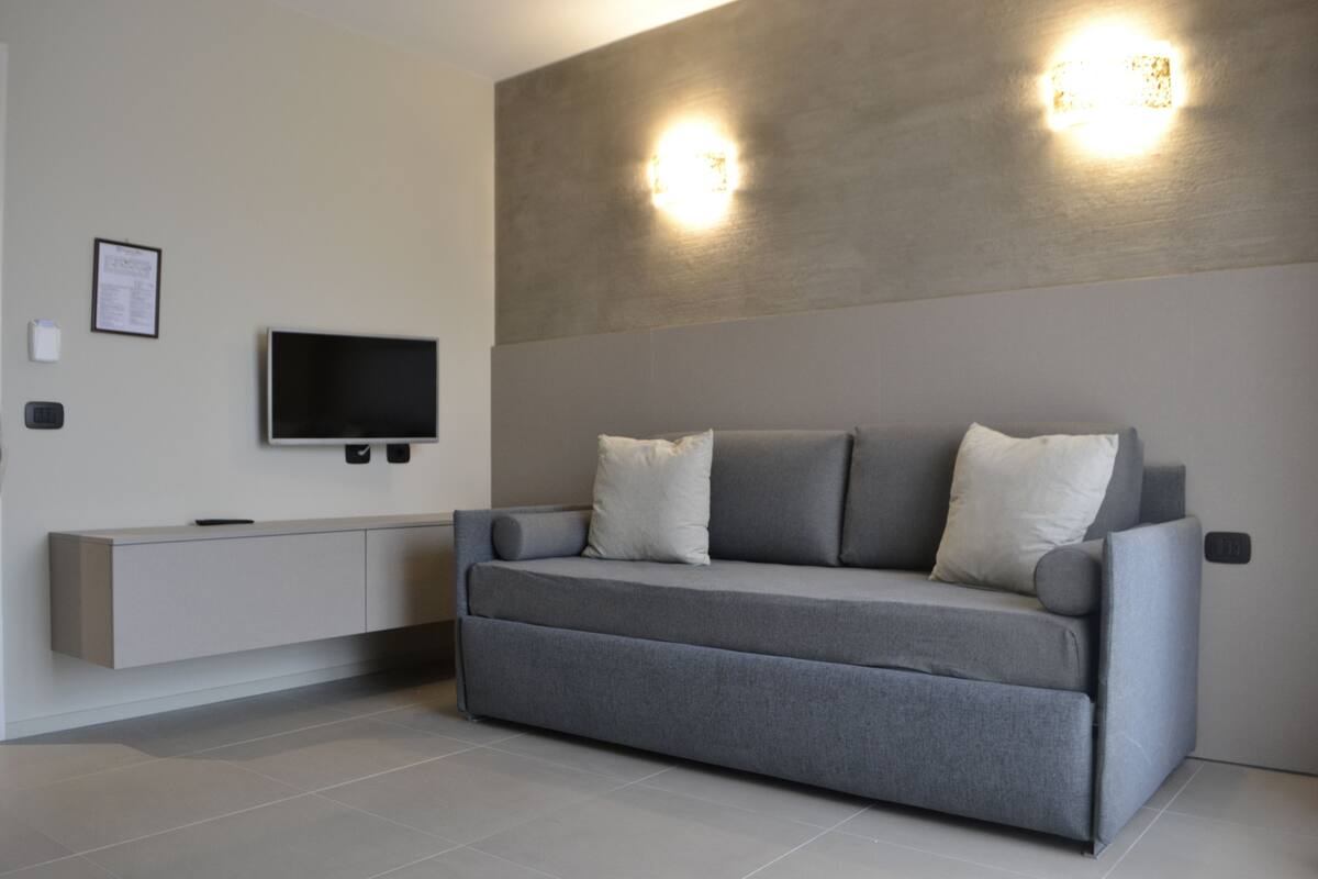 A modern living room with a grey sofa, two wall-mounted lights, a flat-screen TV, and a minimalist console unit.