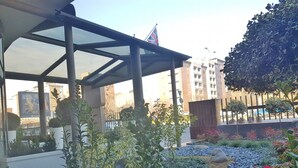 A covered outdoor area with a glass roof, surrounded by greenery and red flowers. - Plus Welcome Milano (Milan)