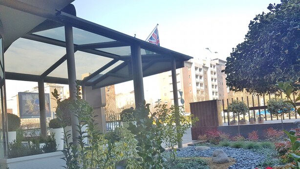 A covered outdoor area with a glass roof, surrounded by greenery and red flowers. - Plus Welcome Milano (Milan)