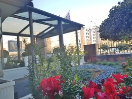 A covered outdoor area with a glass roof, surrounded by greenery and red flowers.
