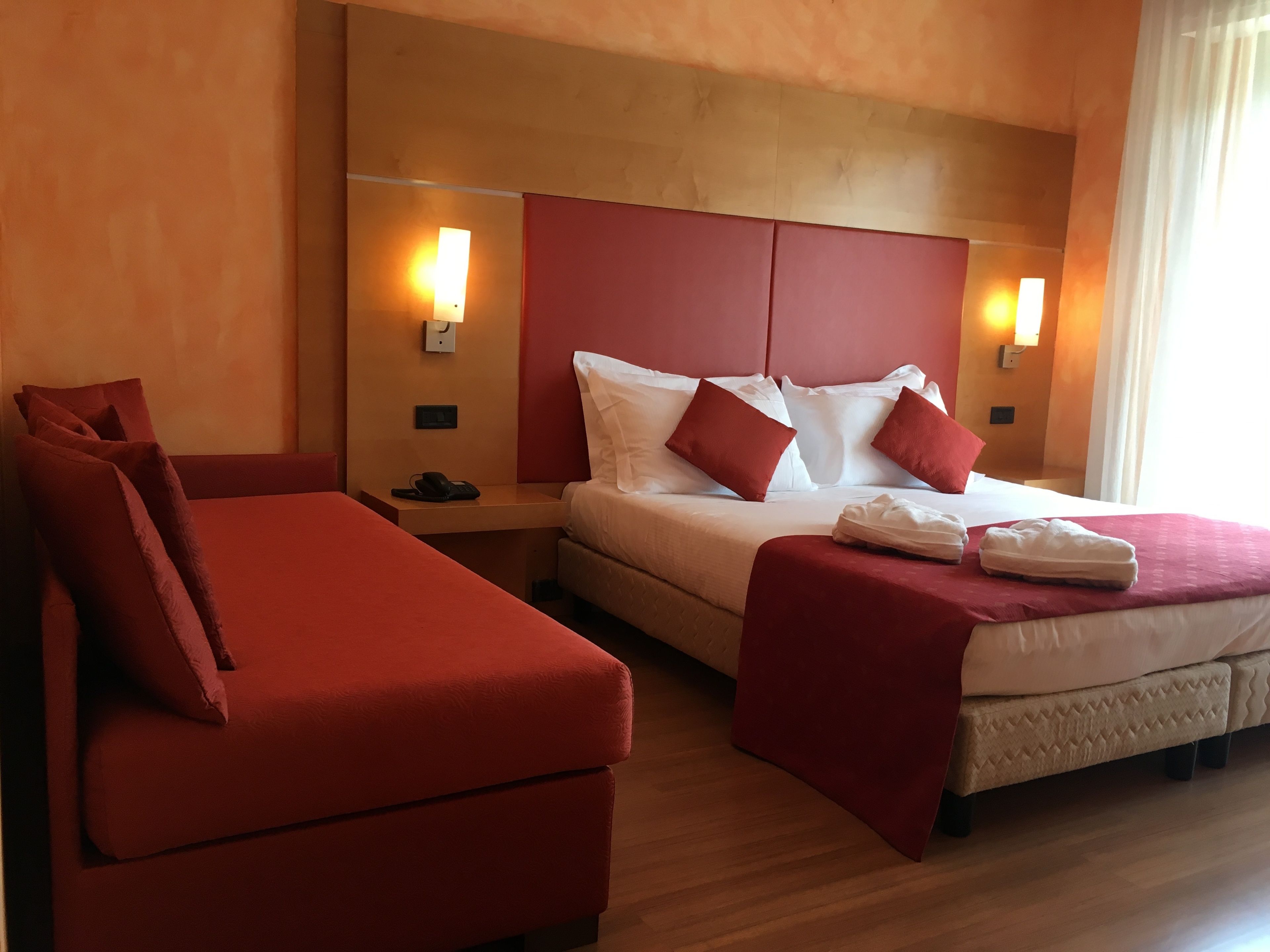 Een hotelkamer met een bed, een rode bank en twee nachtkastjes met lampen.