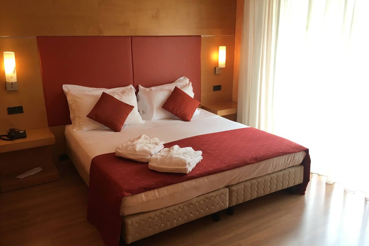 A neatly made bed with white and red bedding, a wooden headboard, and two bedside lamps.