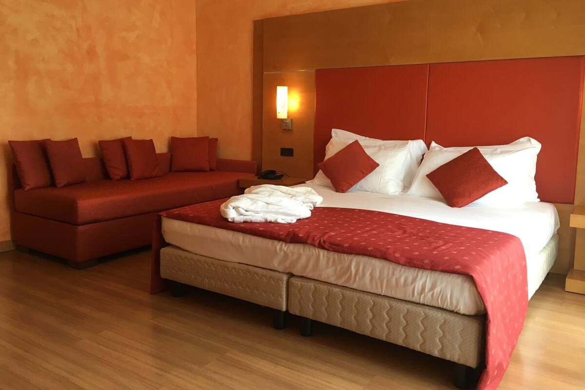 A hotel room with a bed, a sofa, and a nightstand.