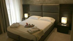 A modern hotel room with a large bed, two bedside tables with lamps, a tray with breakfast items, and a view of the outdoors through sheer curtains. - Plus Welcome Milano (Milan)