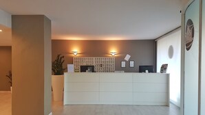 A reception area with a white reception desk, a wall-mounted calendar, and two wall-mounted lights. - Plus Welcome Milano (Milan)