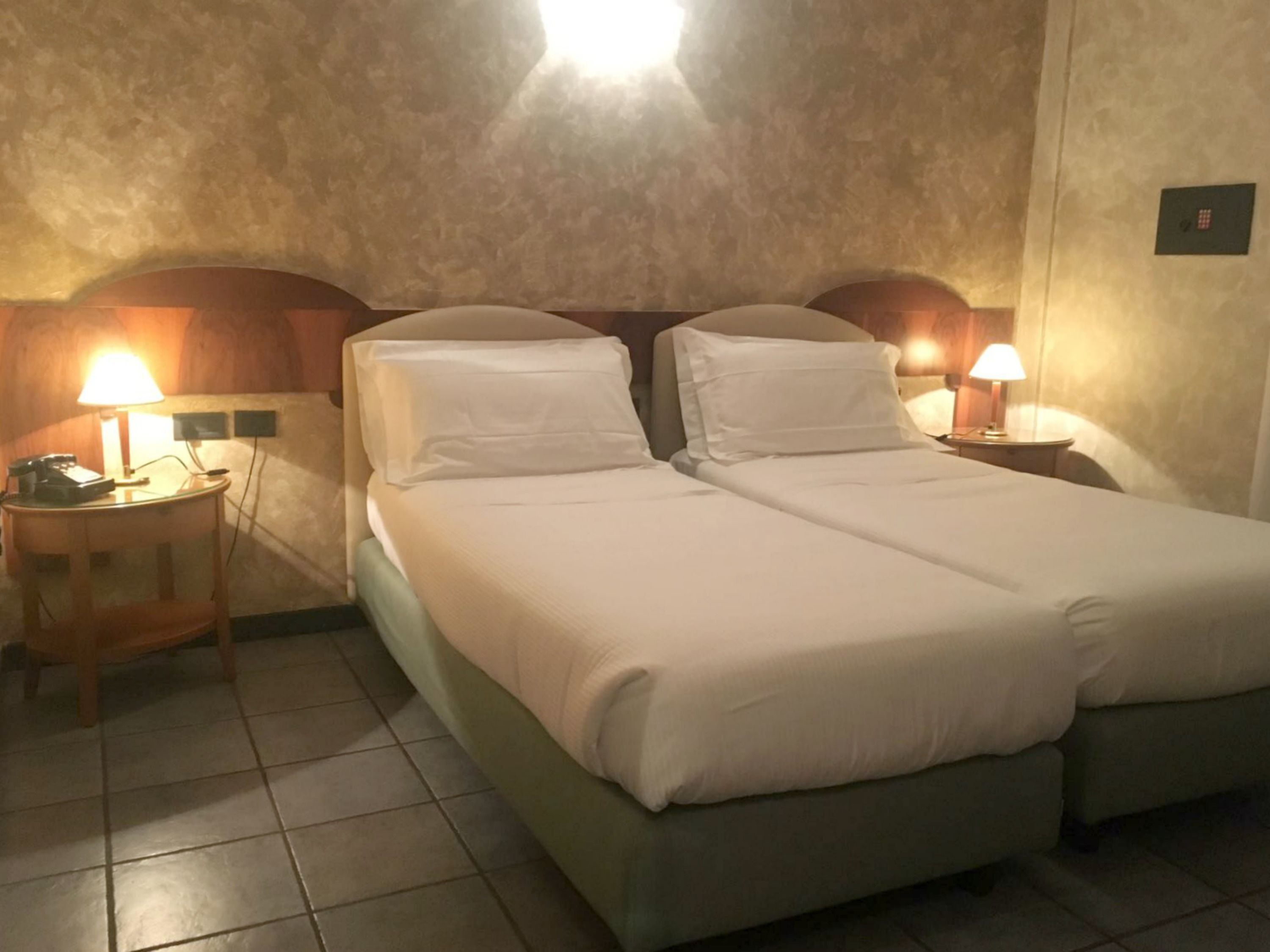 A double bed with white bedding, two bedside tables with lamps, and a wall-mounted light fixture.