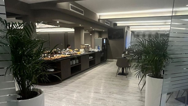 A modern hotel lobby with a long reception desk, potted plants, and a flat-screen TV mounted on the wall. - Plus Welcome Milano (Milan)