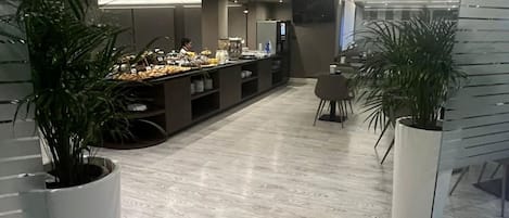 Un moderno vestíbulo de hotel con un largo mostrador de recepción, plantas en macetas y un televisor de pantalla plana montado en la pared.