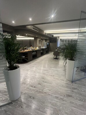 Un moderno vestíbulo de hotel con un largo mostrador de recepción, plantas en macetas y un televisor de pantalla plana montado en la pared.