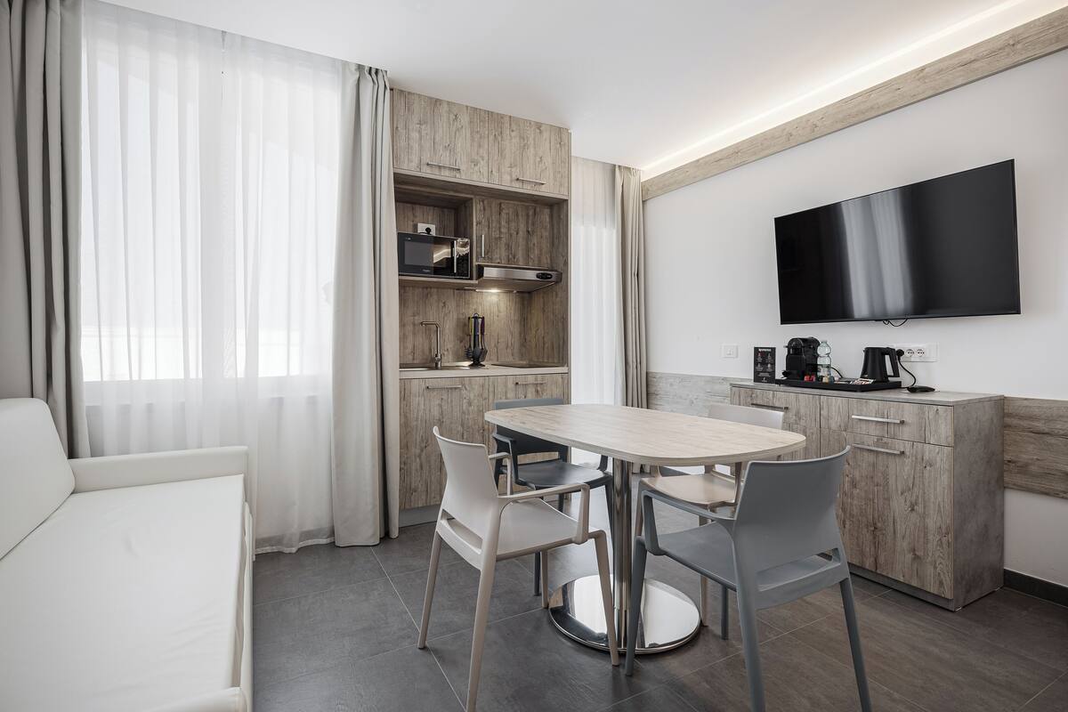 Una habitación de hotel moderna con zona de comedor, kitchenette y televisor de pantalla plana.